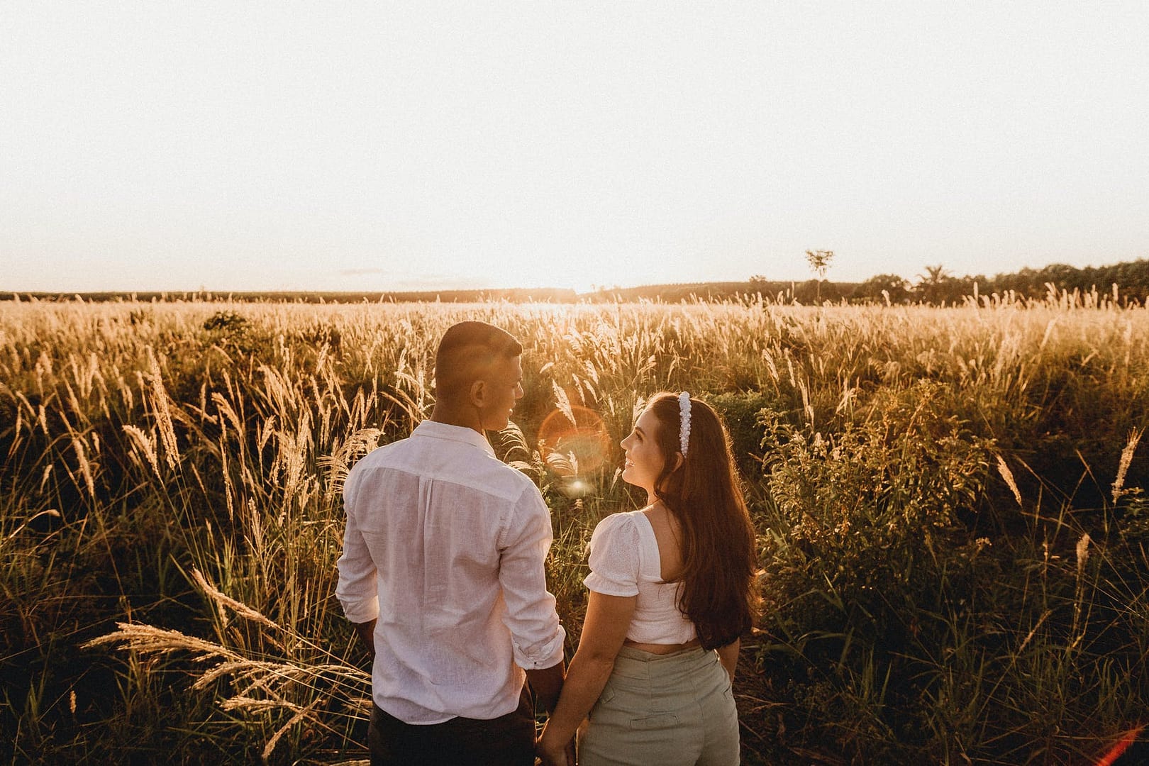 carefree multiethnic couple enjoying romantic sunset in field